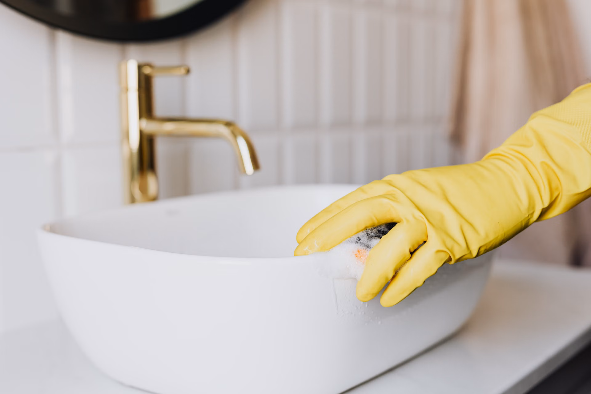 Yellow-gloved hand scrubbing a white sink basin